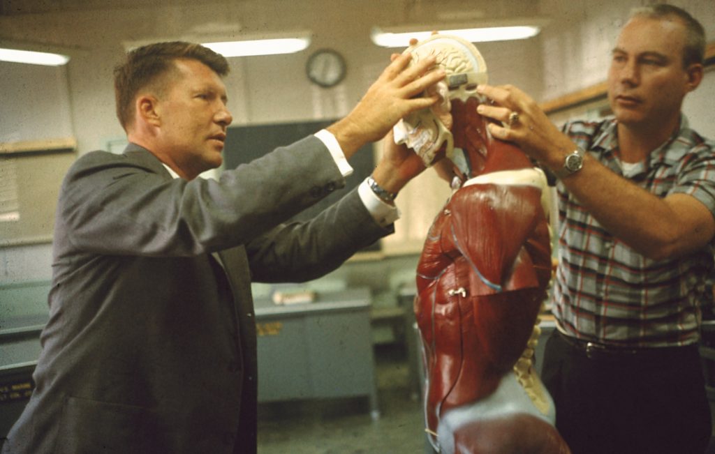 Air Force medical officer Dr. William Douglas giving a physiology lesson to Project Mercury astronaut Walter Schirra, 1959.