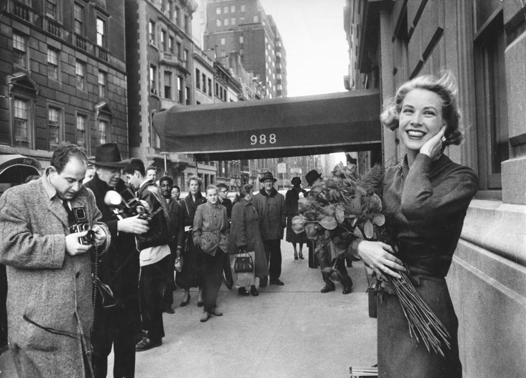 Smiling in a brisk March wind and surrounded by photographers and fans, Grace Kelly poses just off of Fifth Avenue in New York, 1956.