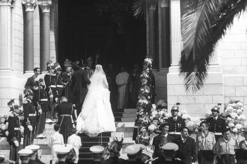 Prince Rainier III and Grace Kelly ascend the steps of Monaco Palace. Kelly's dress required 25 yards of silk taffeta, 100 yards of silk net, 125-year-old rose-point lace bought from a museum, and thousands of tiny pearls.