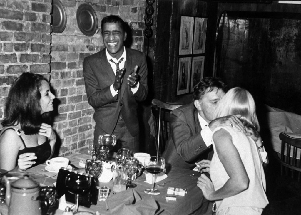 In a New York pub, Sammy applauds as Richard Burton kisses May, Elizabeth beams.