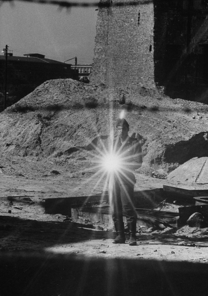 An East German policeman uses sunlight reflected off a mirror in an attempt to stop photographers from taking pictures.