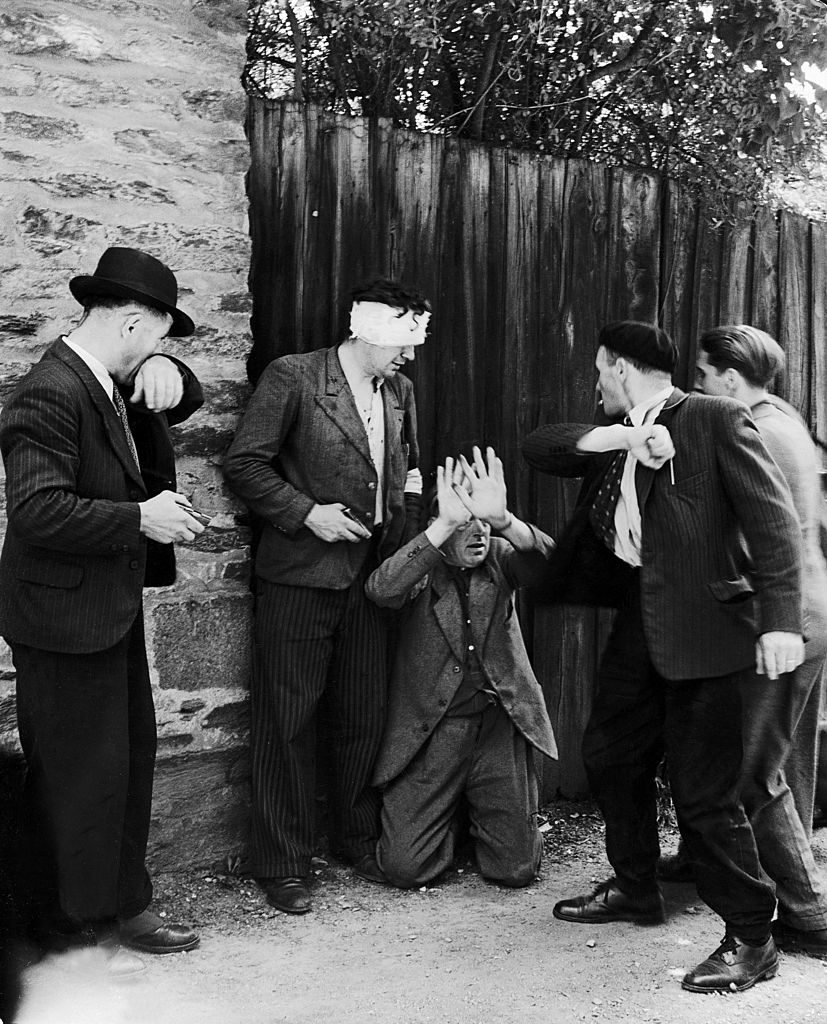 Two Frenchmen train guns on a collaborator who kneels against a wooden fence with his hands raised while another man cocks an arm to hit him, Rennes, France, late August 1944. (Photo by Bob Landry/The LIFE Picture Collection © Meredith Corporation)